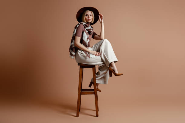 Woman in stylish DIY outfit posed on a stool, exemplifying customized fashion with a hat and checkered scarf.